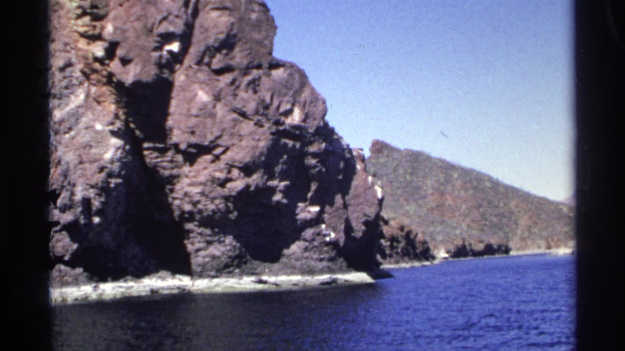 Rocky coastal cliffs beside calm blue water under a clear sky.