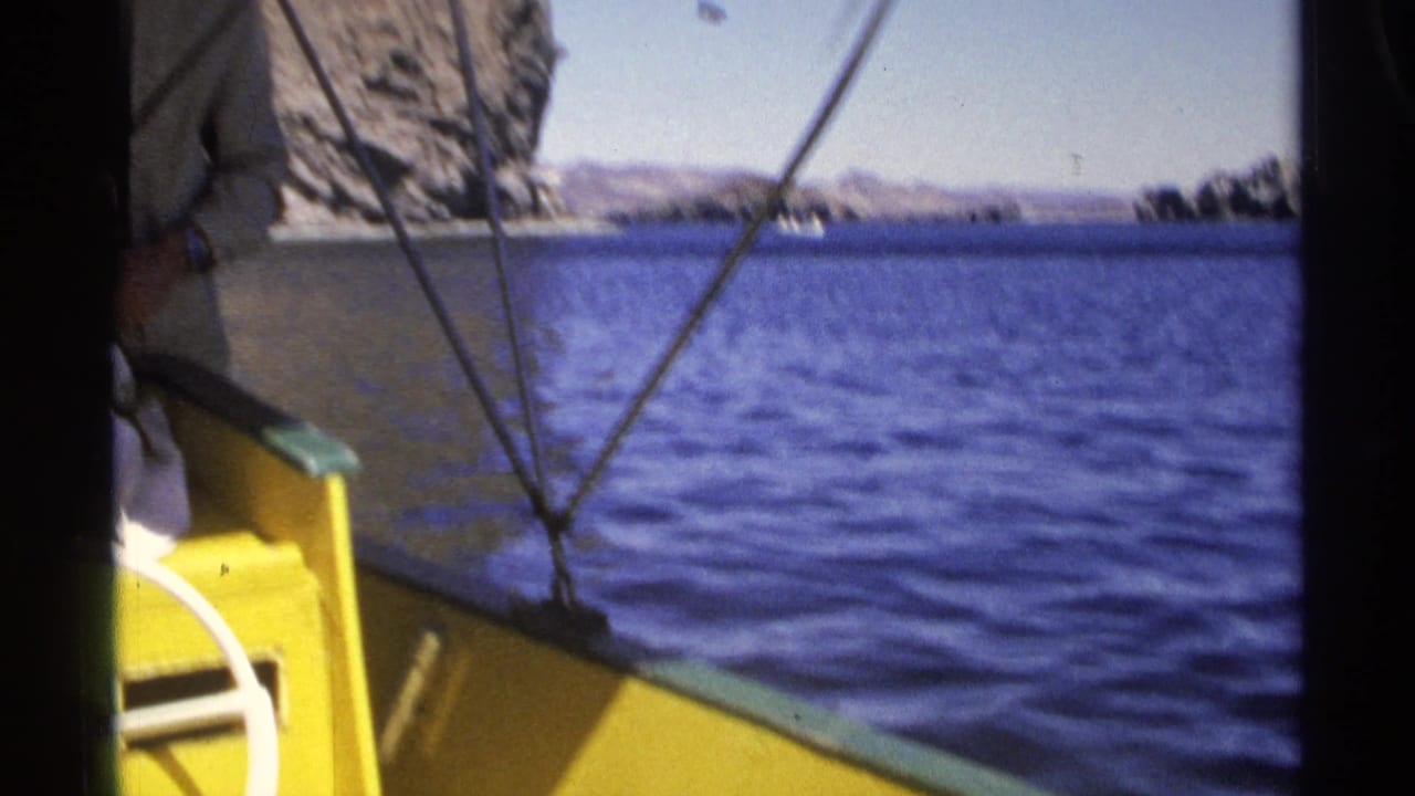 Yellow boat bow on blue water with rocky shoreline in the distance.