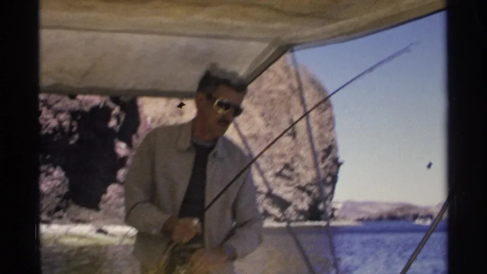 Adult man in sunglasses on a yellow boat in Guaymas, Mexico, handling fishing line with rocky cliffs behind him.