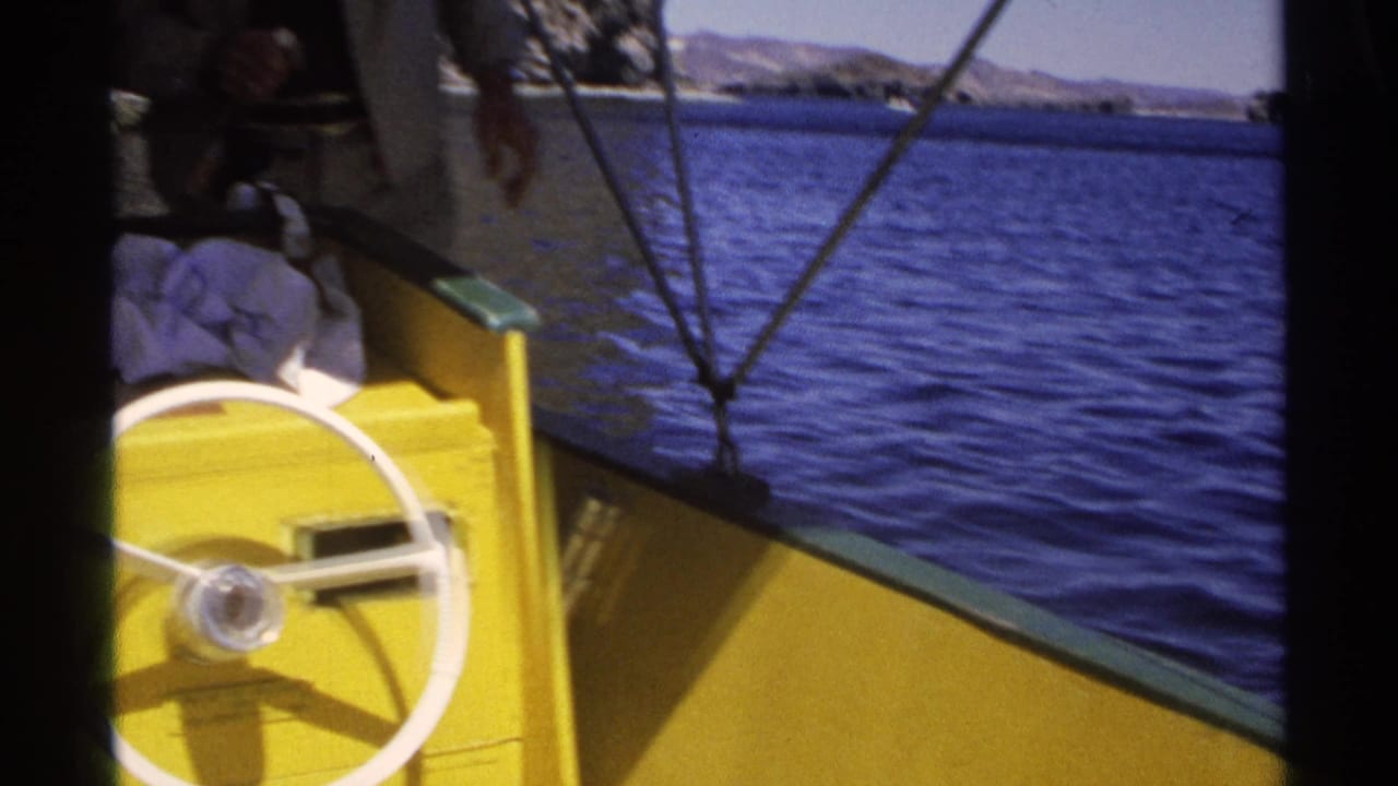 1975 Guaymas home-movie frame showing a yellow boat edge, white steering wheel, blue water, and distant coastal hills.