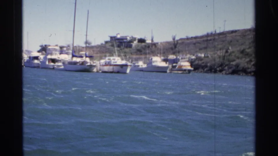 Guaymas, Mexico, 1975 home-movie view of a marina with clustered boats, masts, choppy water, and hillside homes.