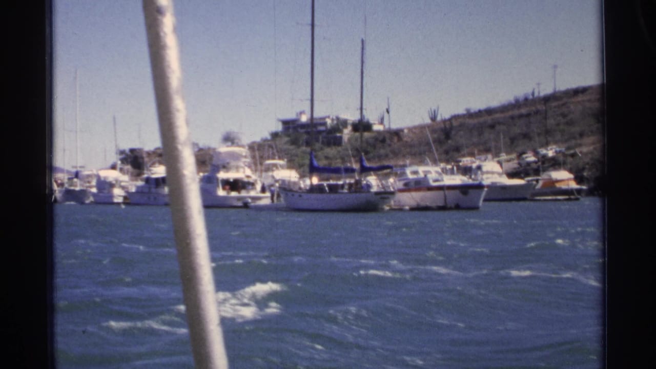 Harbor water, sailboats, motor yachts, and a white mast passing in the foreground.