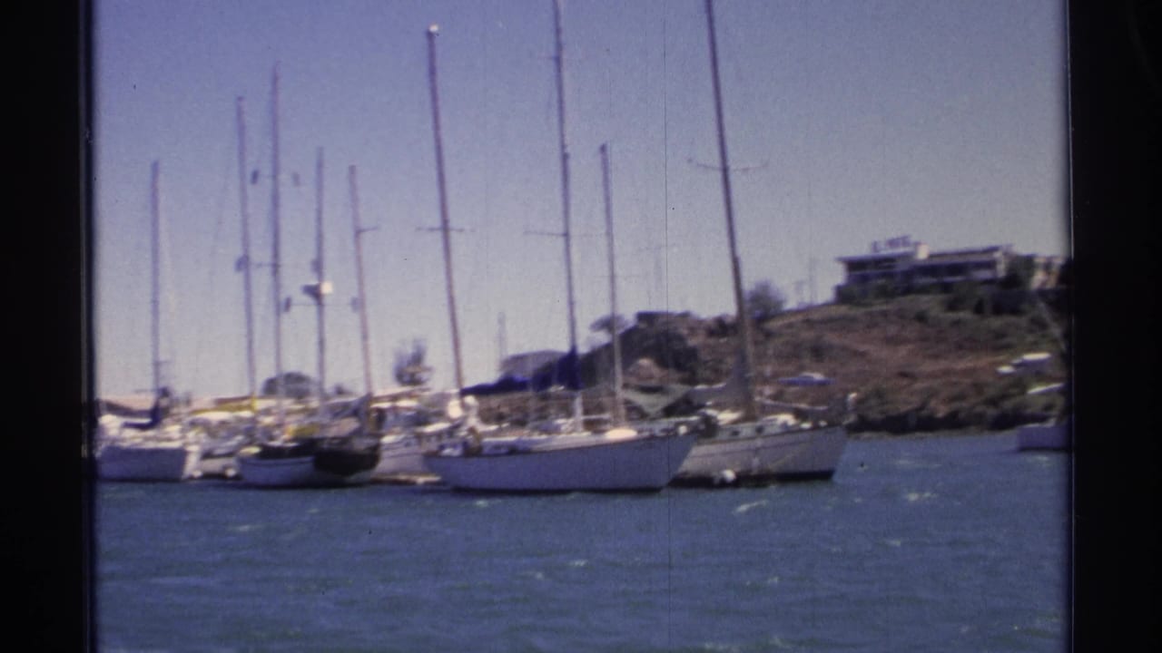 1975 Guaymas marina view with white sailboats, tall masts, blue water, and low buildings on a rocky shore.