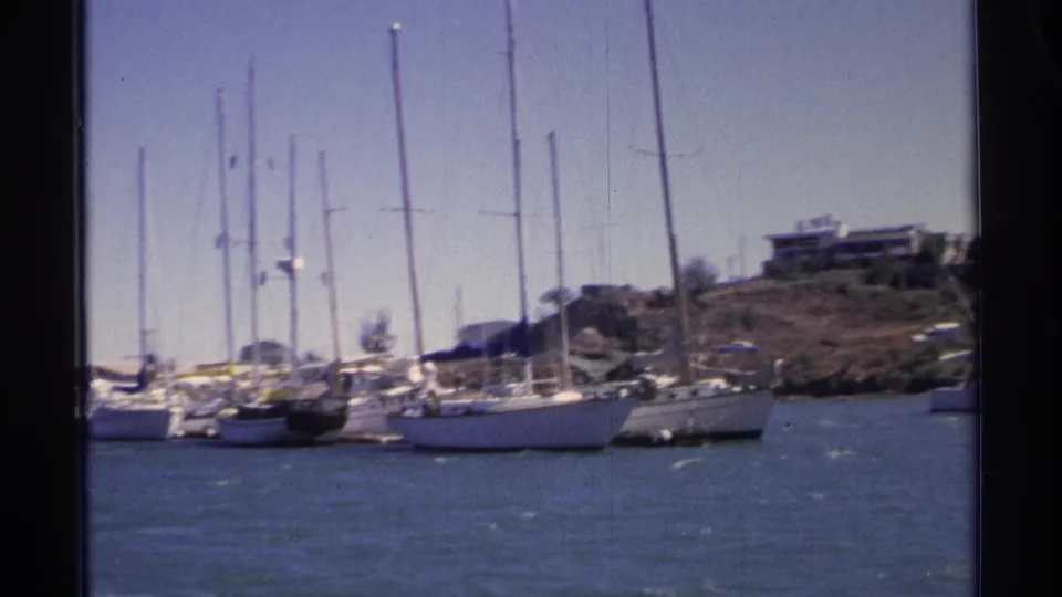 1975 Guaymas marina view with white sailboats, tall masts, blue water, and low buildings on a rocky shore.