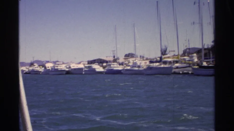 Guaymas marina footage from 1975 showing choppy blue water, moored yachts, sailboat masts, and distant shoreline buildings.