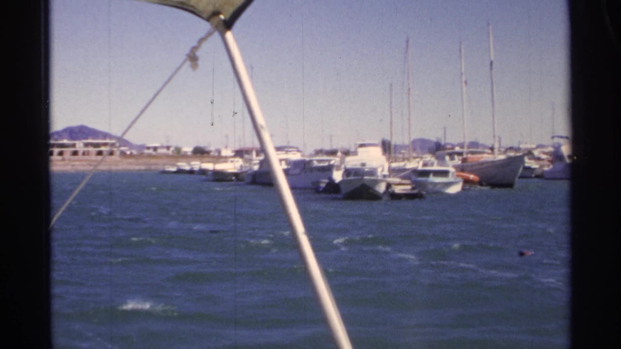 Boats and sailboat masts in a marina viewed past a boat pole over choppy water.