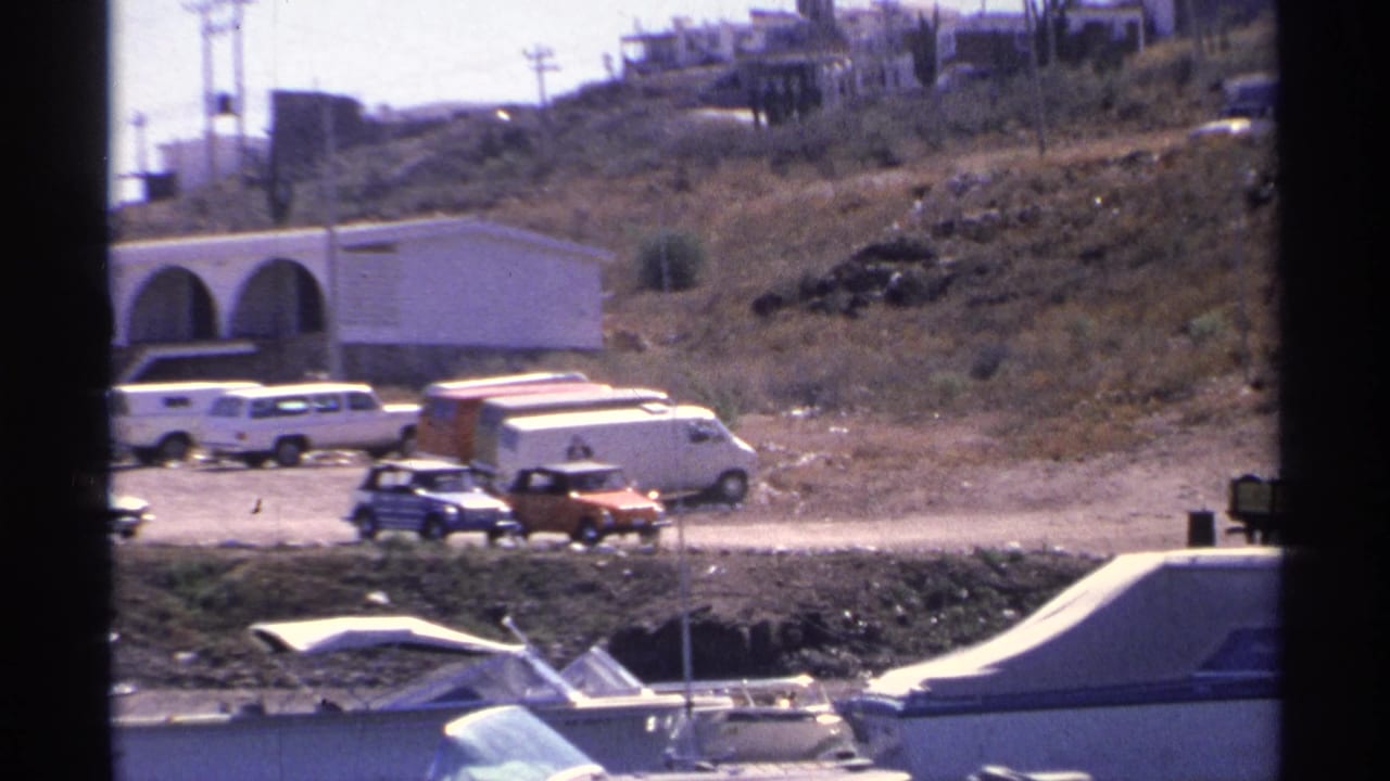Harbor boats pass across the foreground with parked vehicles and arched buildings behind.