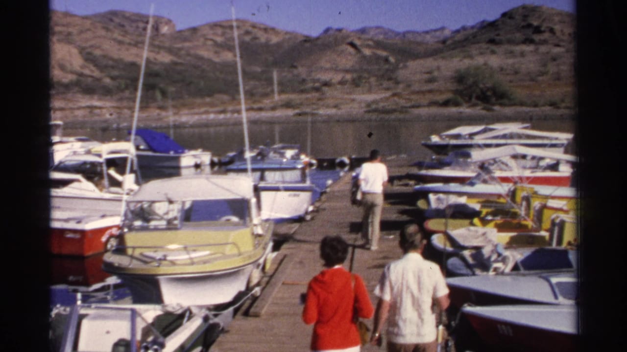 Two adults, including a woman in a red top, appear on the dock as a man walks ahead through the Guaymas marina.