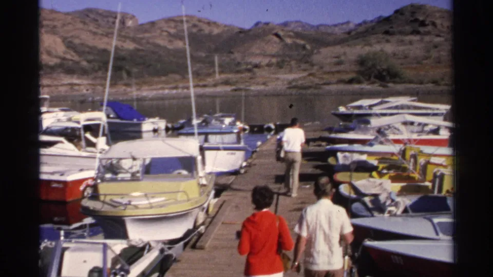 Two adults, including a woman in a red top, appear on the dock as a man walks ahead through the Guaymas marina.
