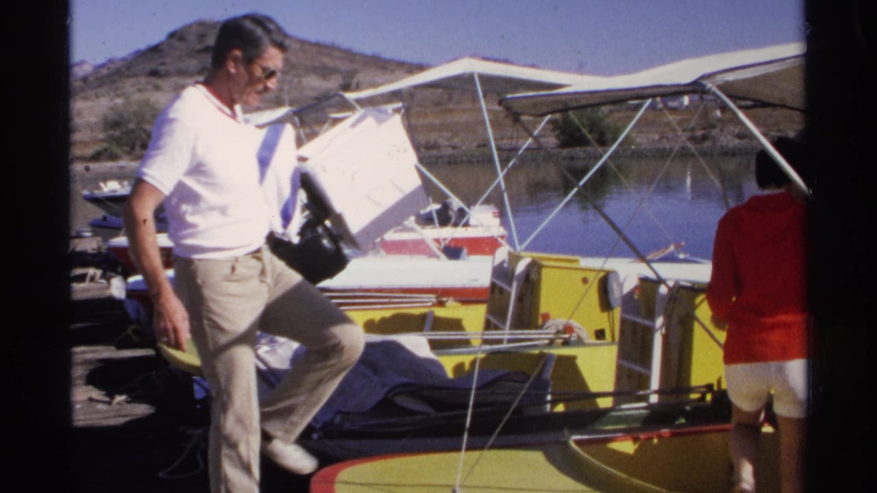In 1975 Guaymas, Mexico, a man carrying a white cooler steps toward a yellow and white boat as a woman in red stands nearby.