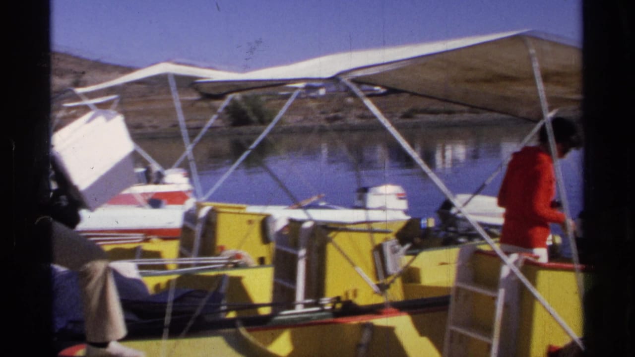 The woman in a red top moves along the yellow and white boat as the man exits the edge of frame, with other moored boats nearby.