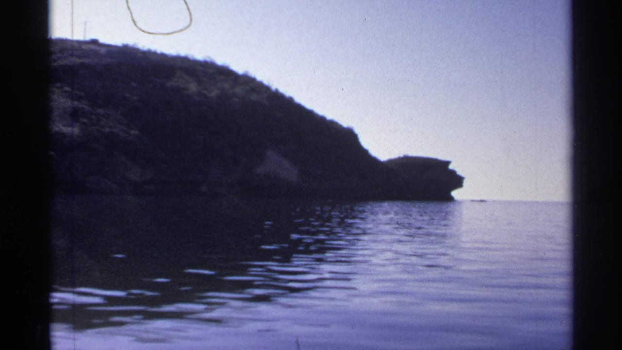 A rocky coastal or lakeside bluff near Guaymas is seen from the water, with gentle ripples and a clear sky.