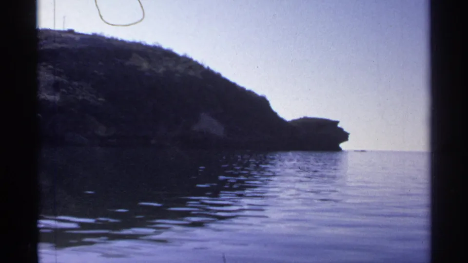 A rocky coastal or lakeside bluff near Guaymas is seen from the water, with gentle ripples and a clear sky.