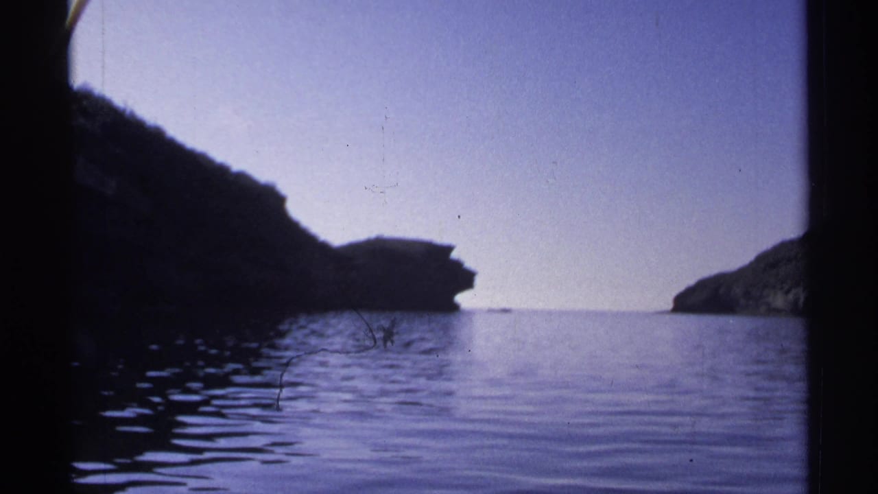 1975 Guaymas home-movie view of a narrow passage between rocky shores, with calm water and faded blue sky.