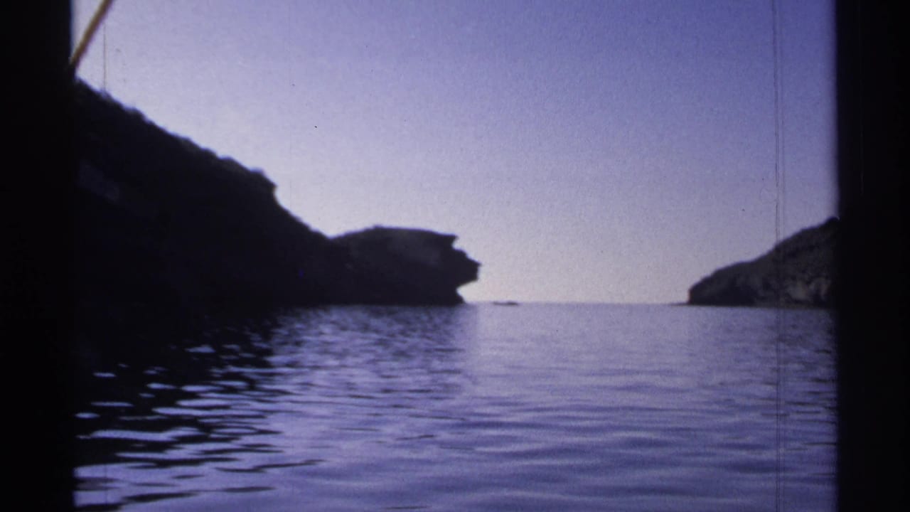 1975 Guaymas frame showing a wide water surface, dark rocky landforms on both sides, and a quiet horizon in soft 8mm color.