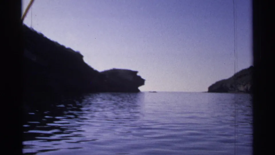 1975 Guaymas frame showing a wide water surface, dark rocky landforms on both sides, and a quiet horizon in soft 8mm color.