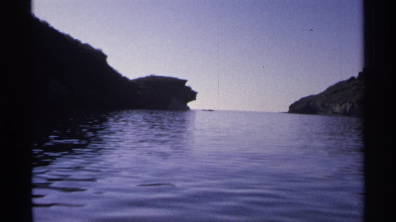 Calm blue water between dark rocky cliffs under a pale sky.