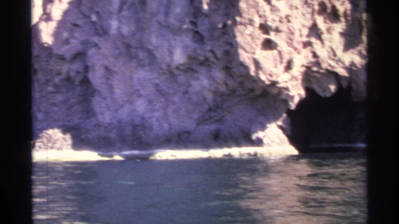Pale cliff wall above calm water with a shadowed cave or recess near the right edge.