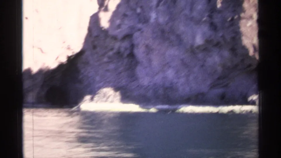 1975 Guaymas 8mm frame showing calm water against a sunlit and shadowed rocky cliff base.