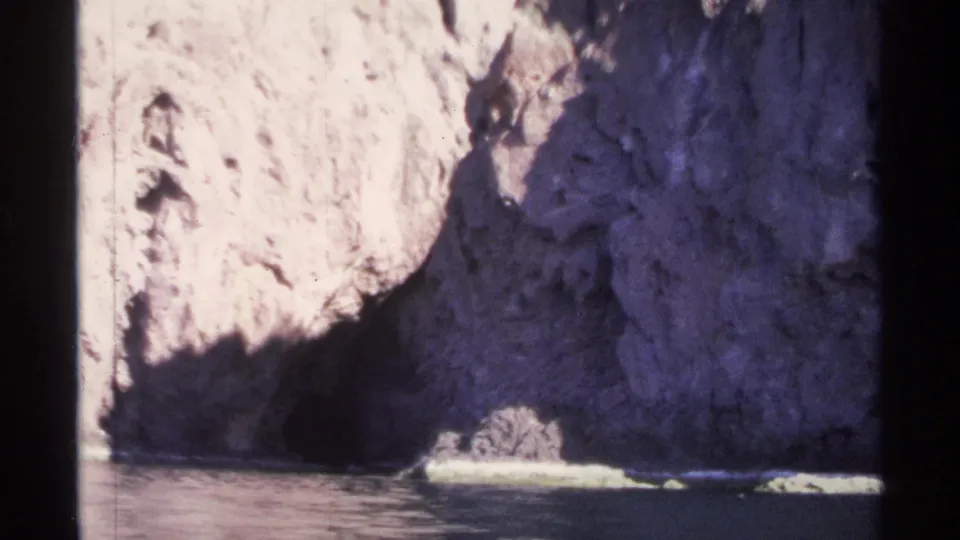1975 Guaymas travel-film frame with a dark cave-like opening set in pale coastal rock above calm water.