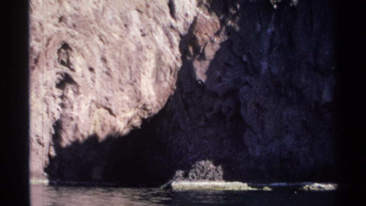 Sunlit rocky cliff above dark coastal water with a pale ledge near the shoreline.