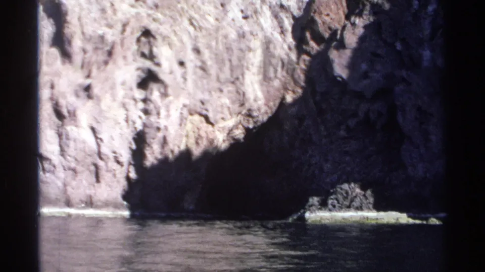 Guaymas, Mexico 1975 home-movie frame showing sunlit stone above a shadowed shoreline and dark water.