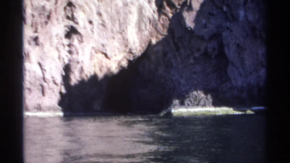 Final 1975 Guaymas frame showing a rugged cliff, deep coastal shadow, and a pale ledge beside still water.