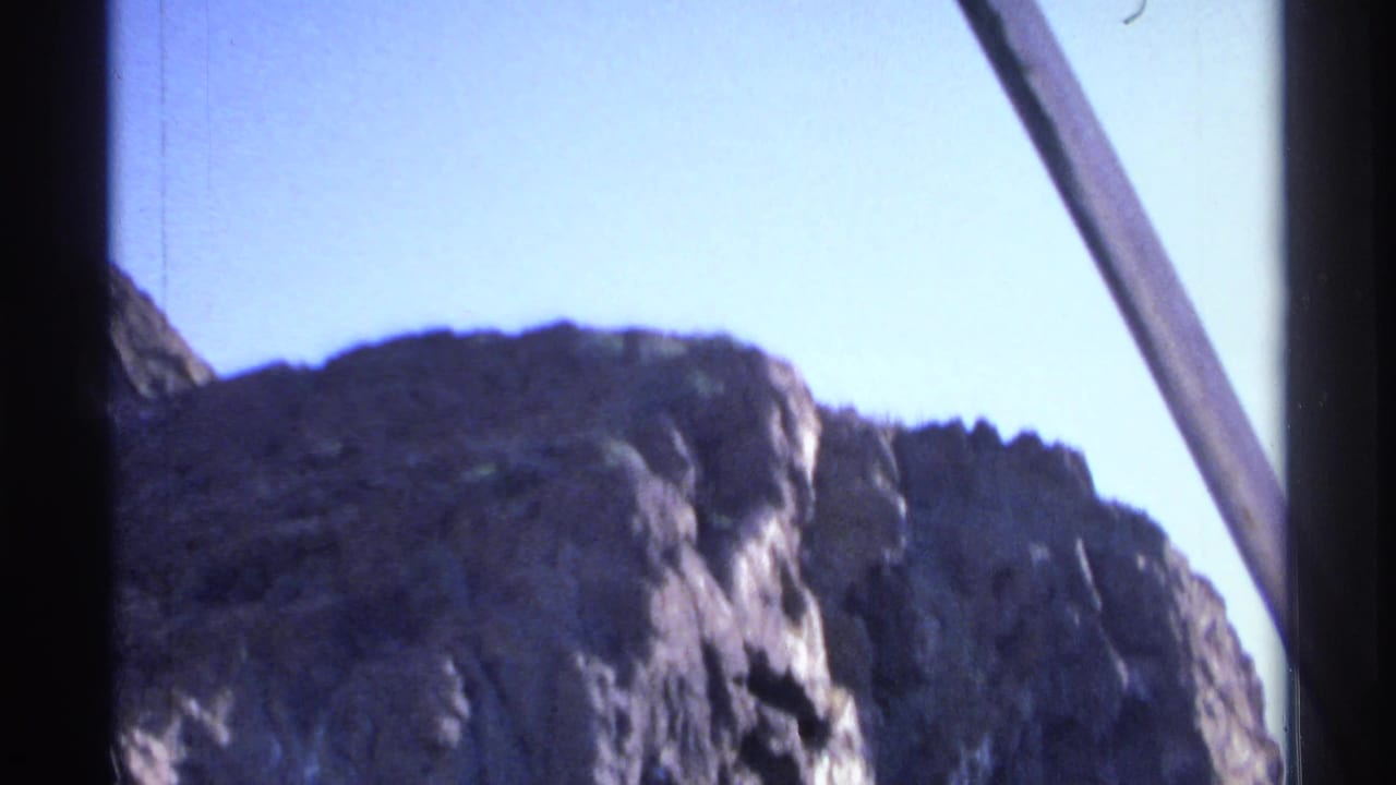 Sunlit cliff ridge under blue sky with a diagonal boat or frame edge visible.