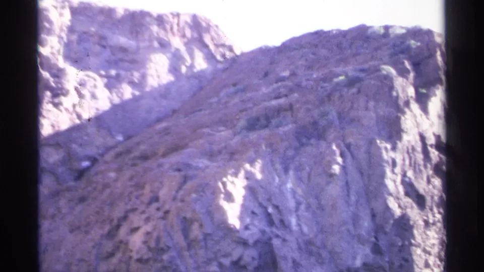 1975 Guaymas coastal cliff seen from below, with washed sunlight, violet film shift, and water at the base.