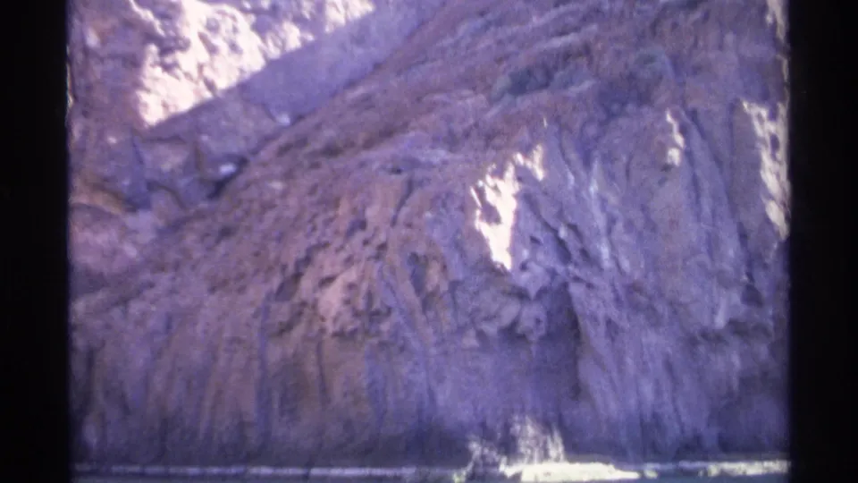 Final 1975 Guaymas frame of a steep coastal rock wall and waterline, tinted by aged 8mm color.