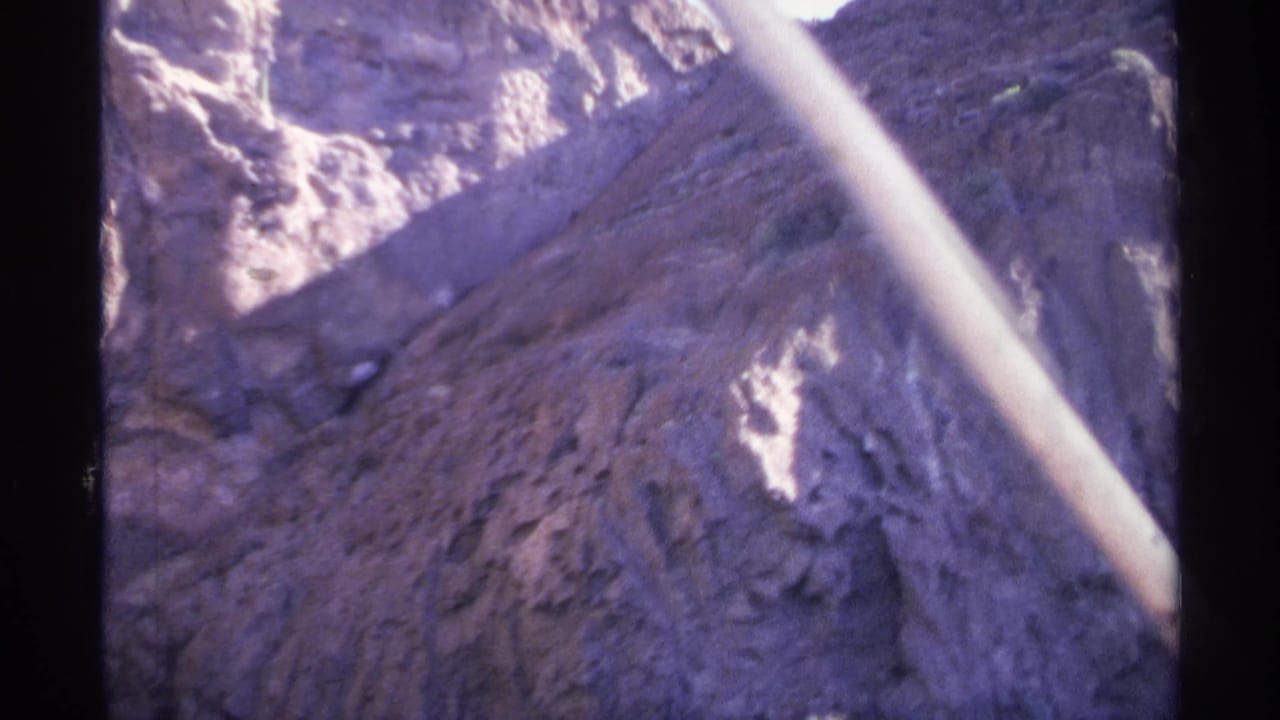 Sunlit canyon wall above dark water, seen through 8mm film-frame borders.