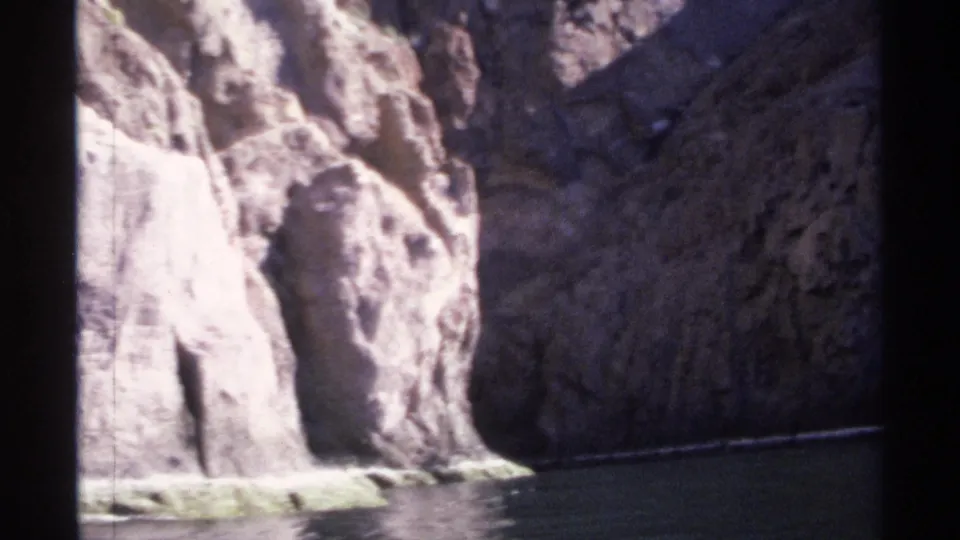 1975 Guaymas canyon footage with calm water at the base of high rock walls, bright sun on one cliff face, and deep shade in the passage.