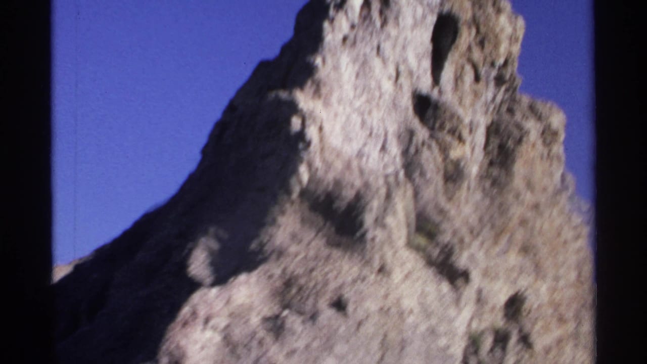 1975 Guaymas 8mm frame with the upper portion of a rugged rock formation set against a clear blue sky.