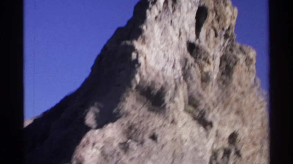 1975 Guaymas 8mm frame with the upper portion of a rugged rock formation set against a clear blue sky.