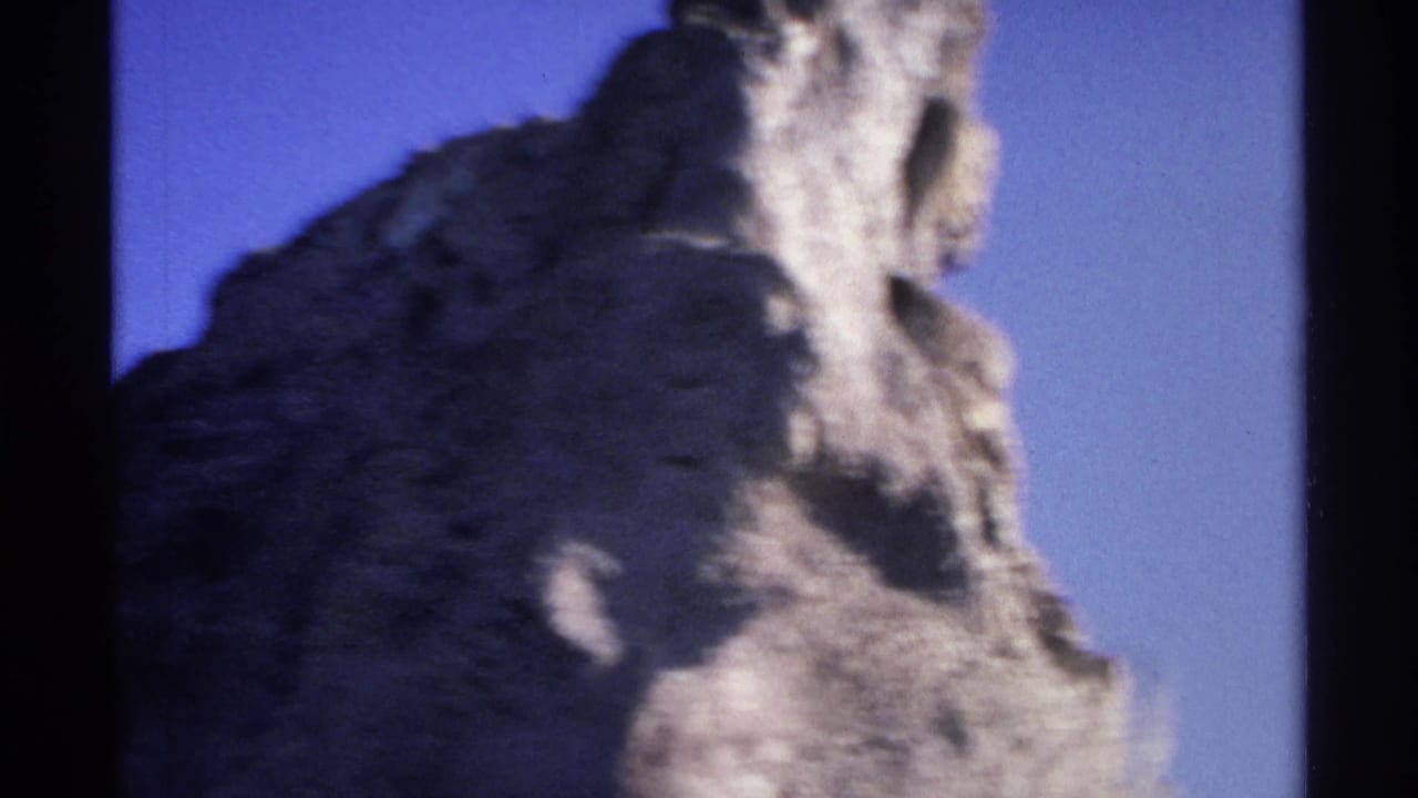Rugged rock formation rising against a blue sky with dark film borders.