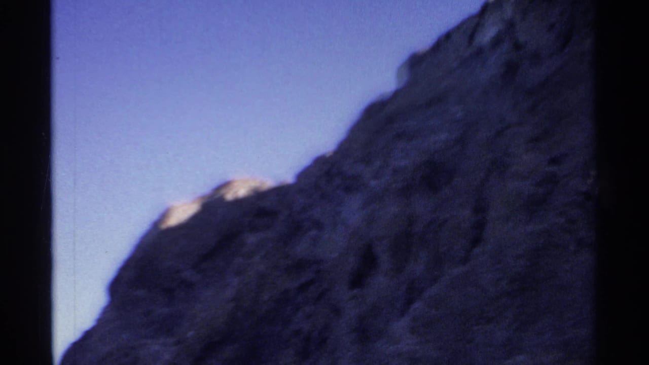 1975 Guaymas travel footage frame with a shadowed rock wall, bright sky, and visible 8mm frame edge.