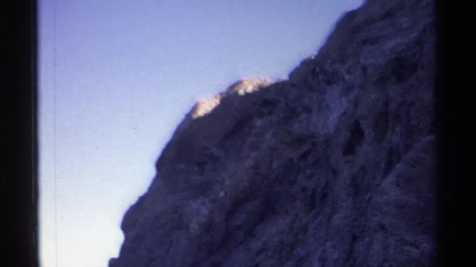 8mm frame from Guaymas in 1975 showing a broad textured rock slope under pale blue sky during a handheld pan.