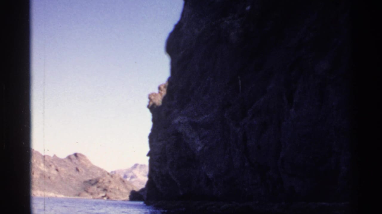Rocky shoreline frames a narrow view of water and distant mountains.