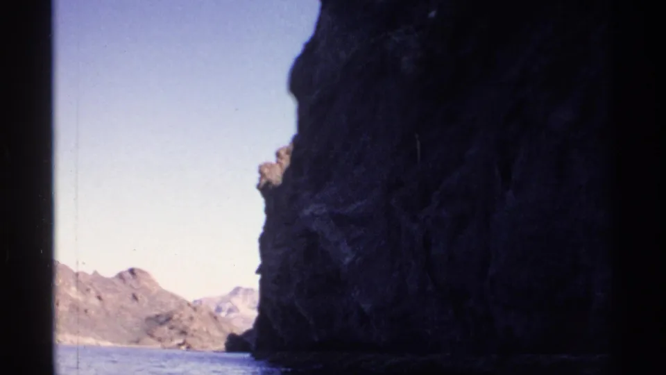 A boat-level view between dark coastal rocks toward distant mountains and water near Guaymas, Mexico.