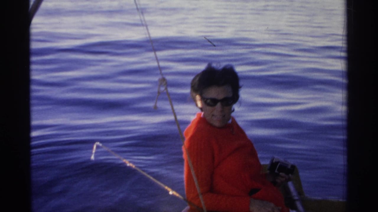 Woman in red sweater and sunglasses seated on a small boat over blue water.