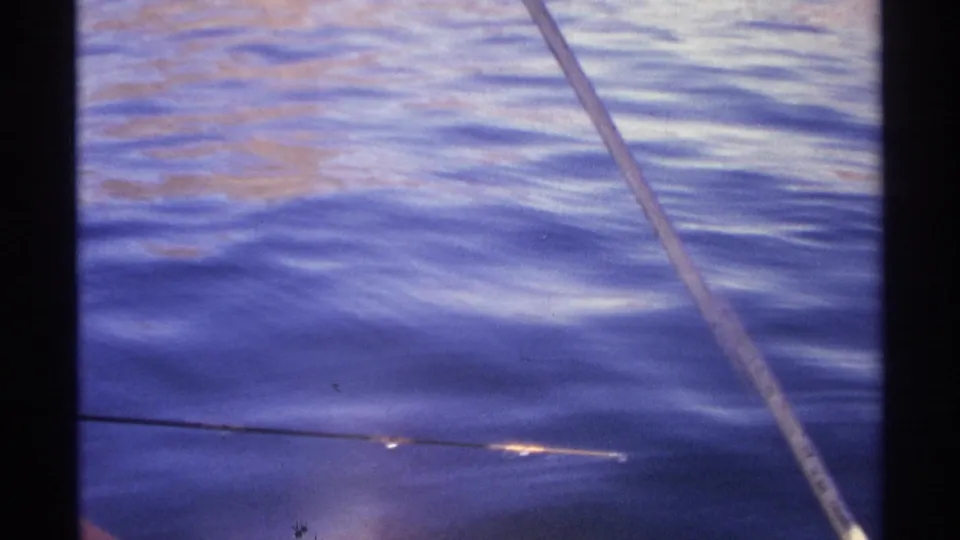 The frame lingers on rippling water beside the boat, with fishing rods crossing the 1975 8mm home-movie frame.