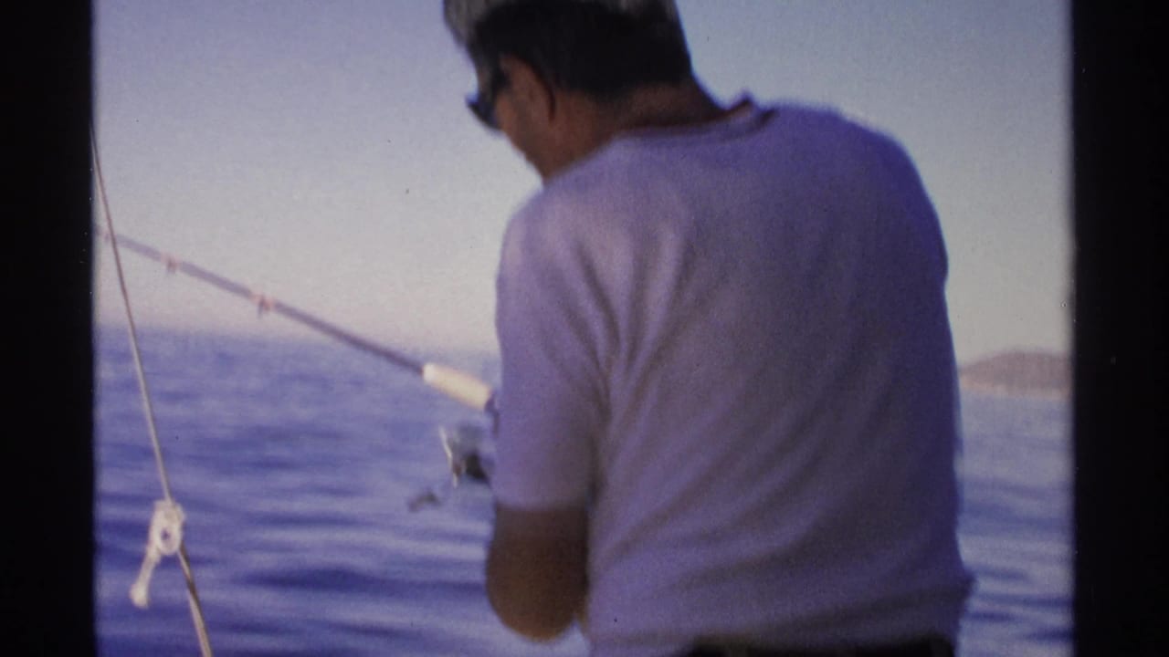 In 1975 Guaymas, Mexico, a man in a white shirt faces away while fishing from a boat on calm sea.