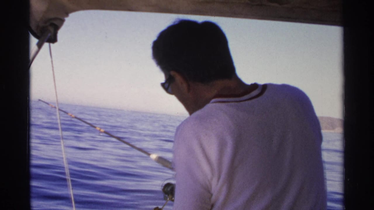 Man in sunglasses leans over a fishing rod on open water.