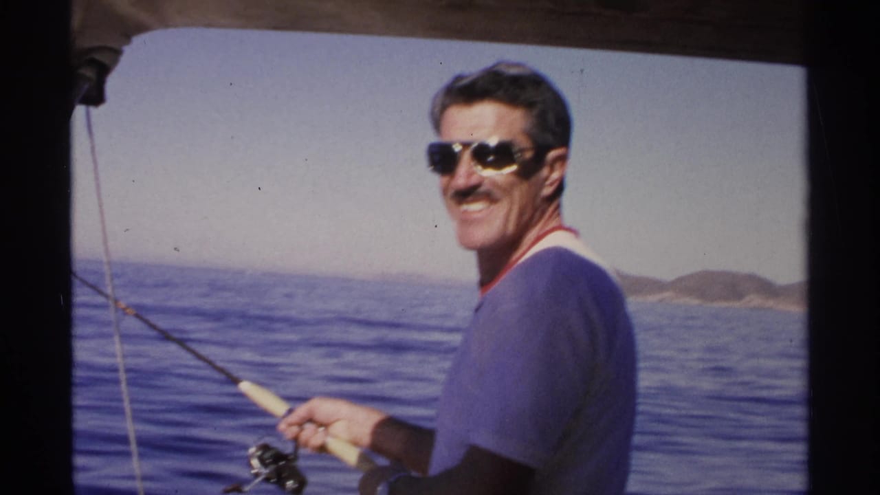 Man in sunglasses smiles while holding a fishing rod on calm blue water.