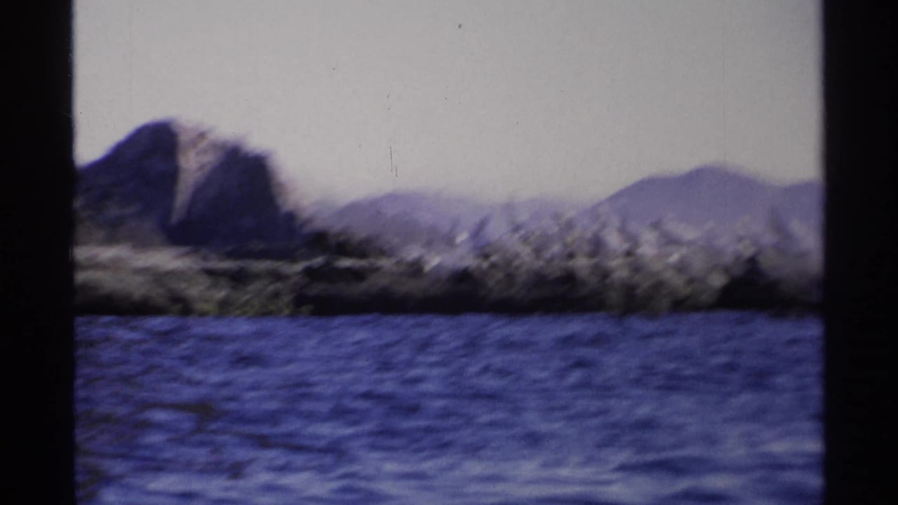 Rocky island and blue water with a large dark mountain form in the background.