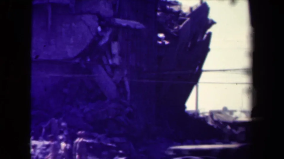 Uniformed men are visible near a damaged building in Manila, with rubble and a pale road below the structure.