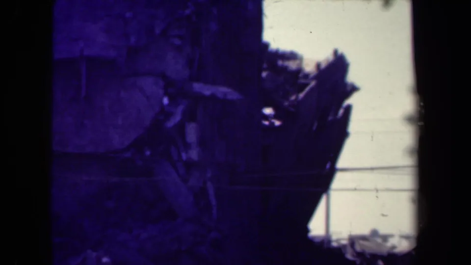 1944 Manila home-movie frame with a broken wooden structure, debris at the base, and visible film edge.