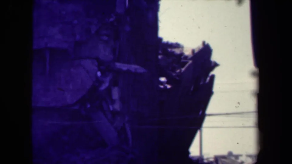 1944 Manila 8mm view of a damaged wooden structure with rubble, sky, and strong blue-purple color shift.