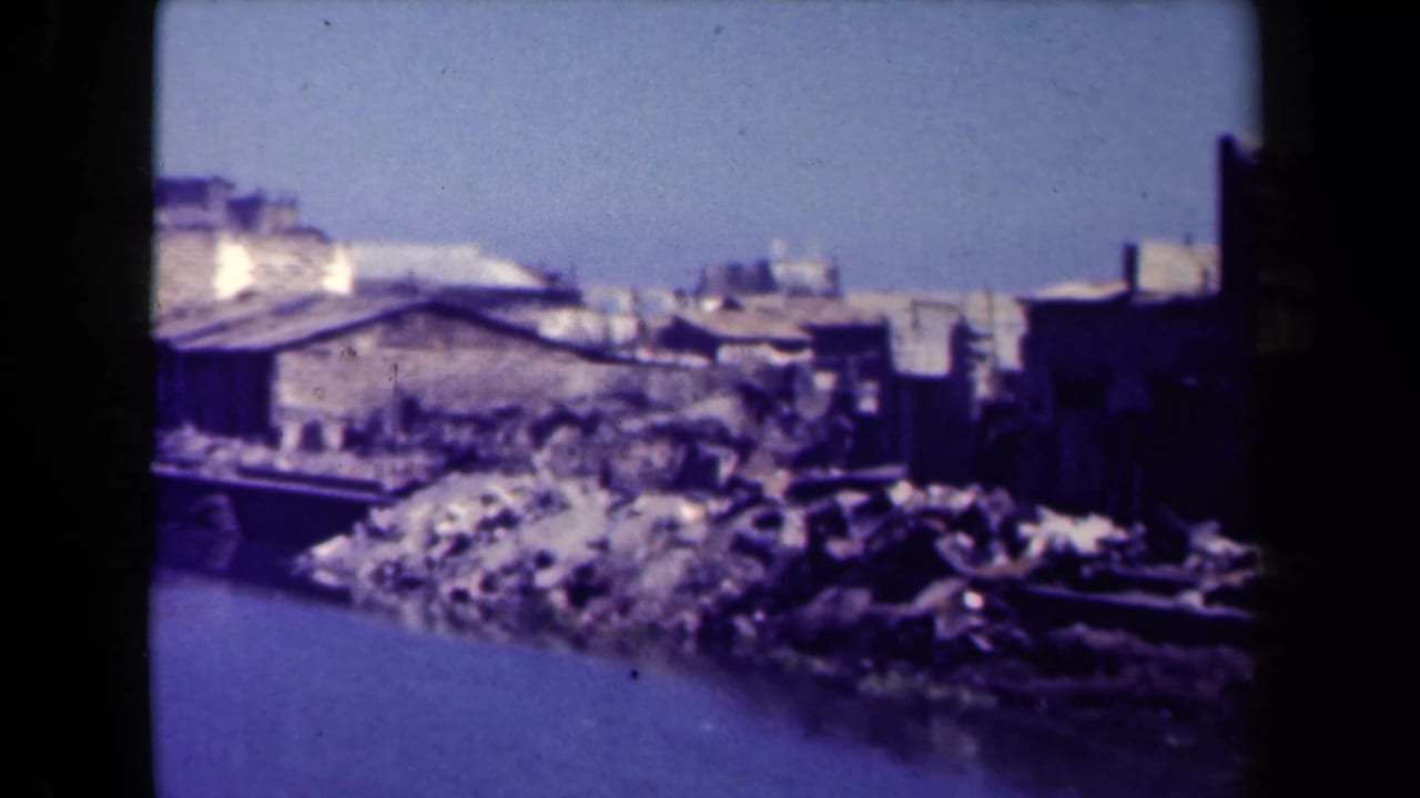 Low riverside structures and debris along still water.