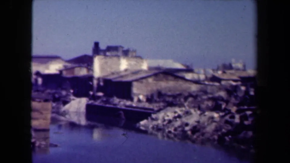 Final 1944 Manila frame showing weathered wooden buildings, shoreline debris, and a calm river beneath a clear sky.